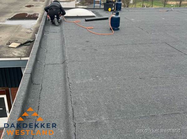 Dakdekker repareert bitumen dakbedekking op groot plat dak in Westland